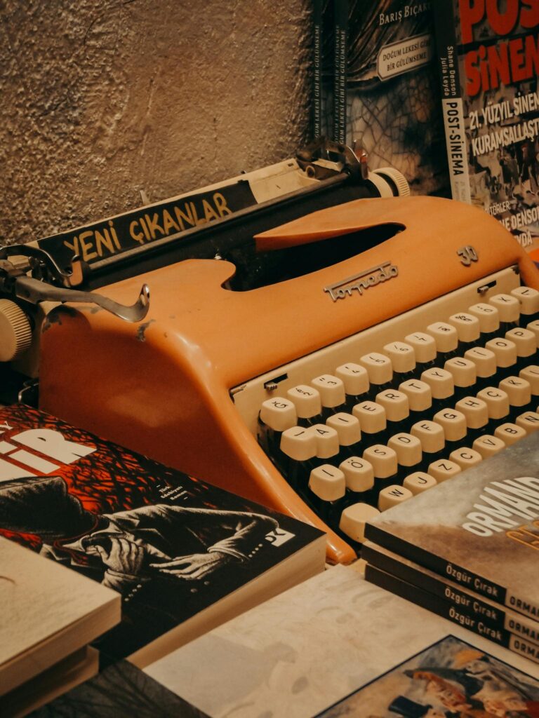 A close-up of a classic orange typewriter with vintage books around it.