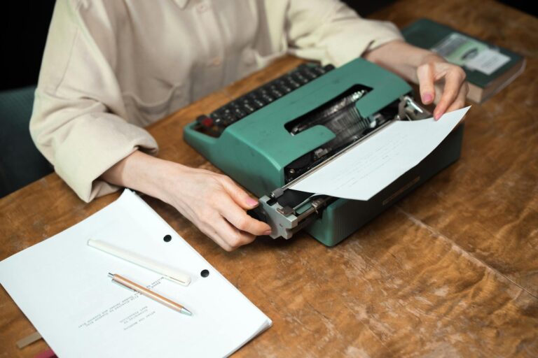 Close-up of hands using a vintage typewriter, with paper and script on a wooden desk.